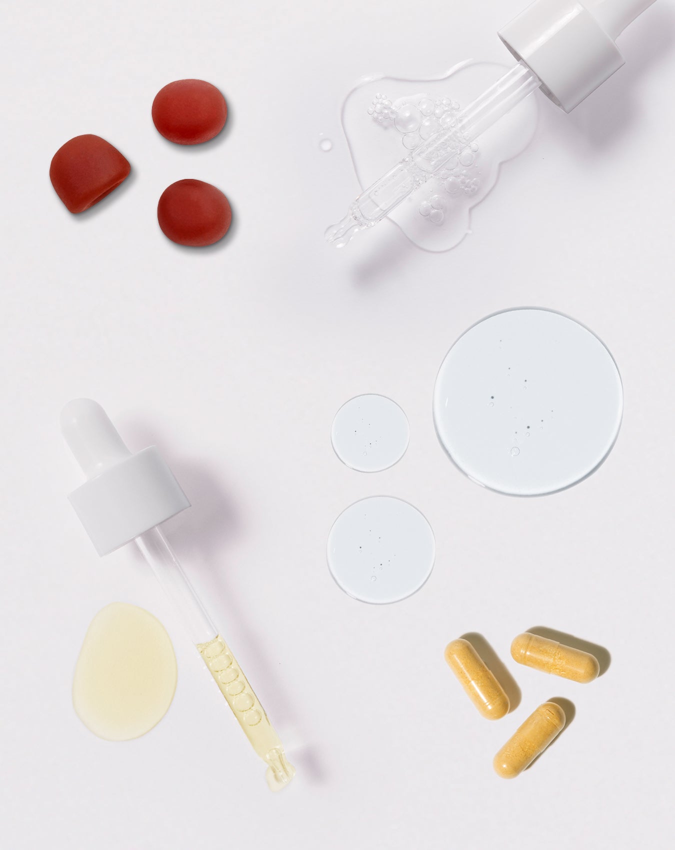Hair gummies, capsules and scalp serum drops arranged on a white background